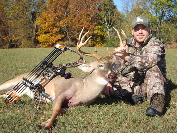 Hunter sitting next to dead deer with bow