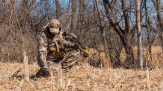 Bowhunter kneeling down to look at cut corn field.