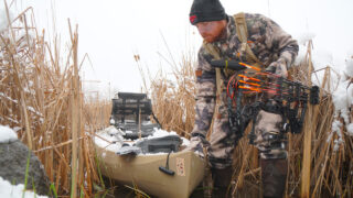 Bowhunter pulling a snow-covered kayak through a swamp.