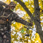 bowhunter at full draw in a tree with yellow leaves during the fall