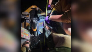 Overhead view of a fishing kayak deck at night showing emergency personnel treating an angler whose foot is pinned to the floorboard by a thin arrow shaft.