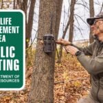 An editorial graphic showing Todd Graf wearing face paint and a camo hat while strapping a cellular trail camera to a tree in an autumn woods. On the left side, a green sign features white text that reads WILDLIFE MANAGEMENT AREA PUBLIC HUNTING IOWA DEPARTMENT OF NATURAL RESOURCES.